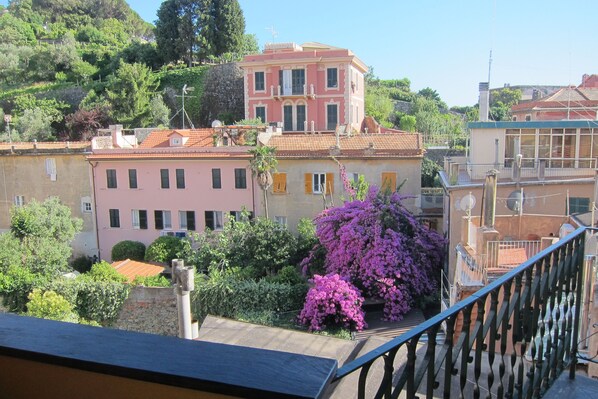 A multi-story building with balconies, surrounded by lush greenery and flowering plants.