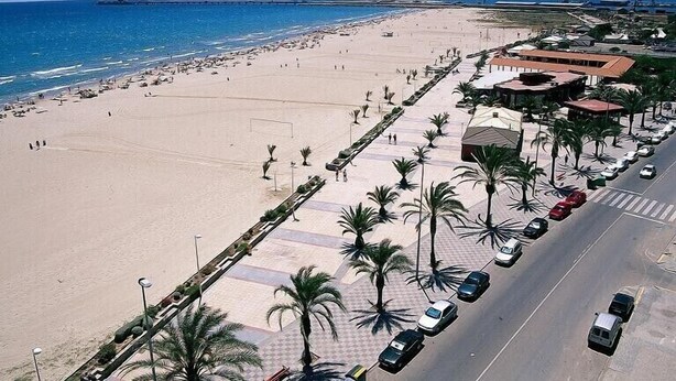 Une plage avec une promenade pavée bordée de palmiers et de voitures garées.