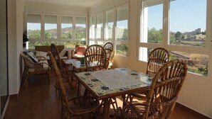 Un coin repas lumineux, avec une table et des chaises, et de grandes fenêtres donnant sur la campagne.