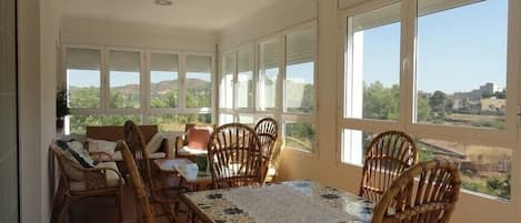 A sunlit dining area with a table and chairs, large windows offering a view of the countryside.