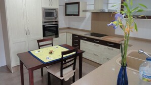 Une cuisine compacte avec des meubles blancs, un four à micro-ondes, un four traditionnel, une cuisinière à gaz et une petite table à manger avec des chaises.