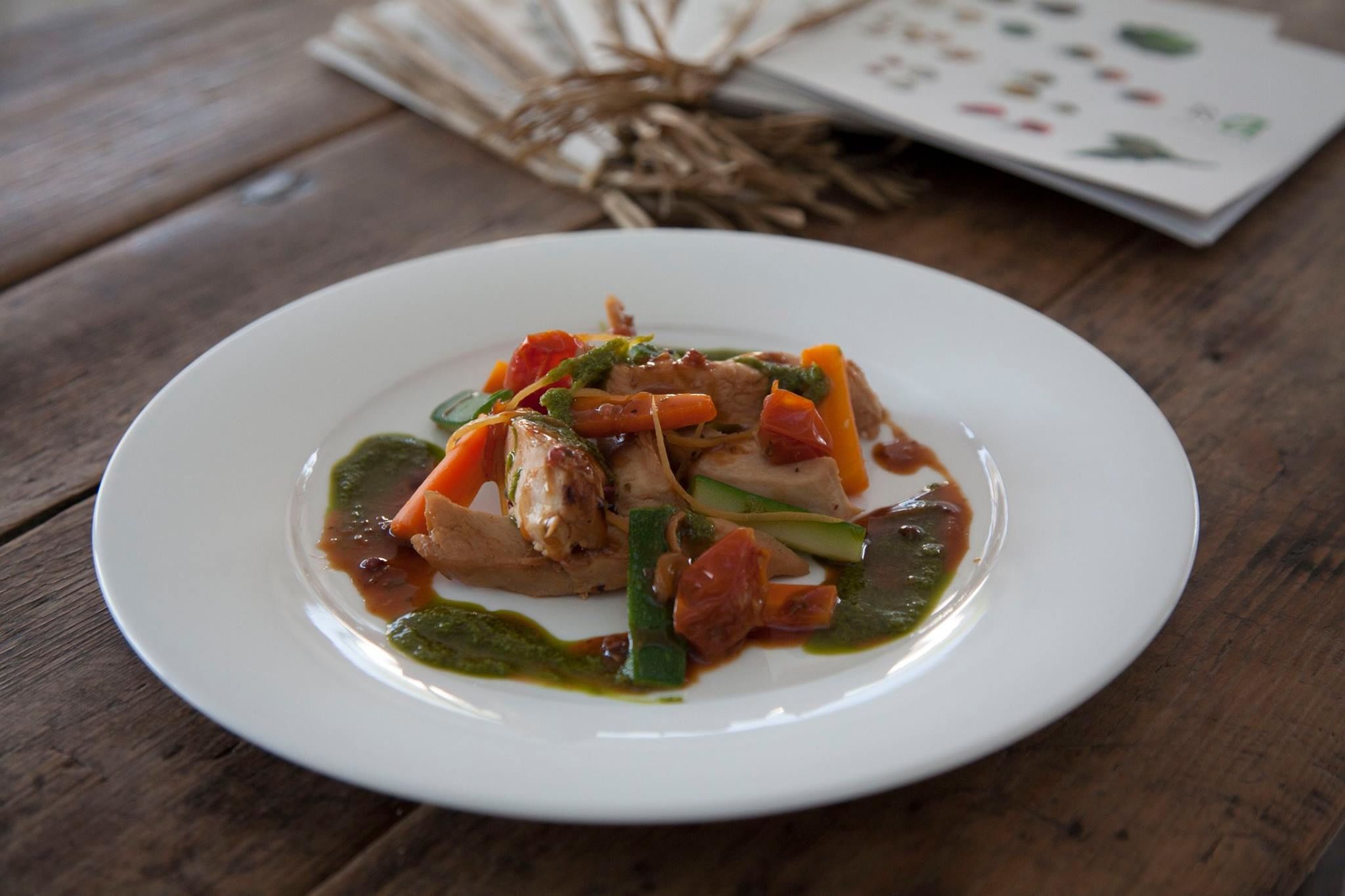 Un piatto bianco con un'insalata di pollo e verdure su un tavolo di legno.
