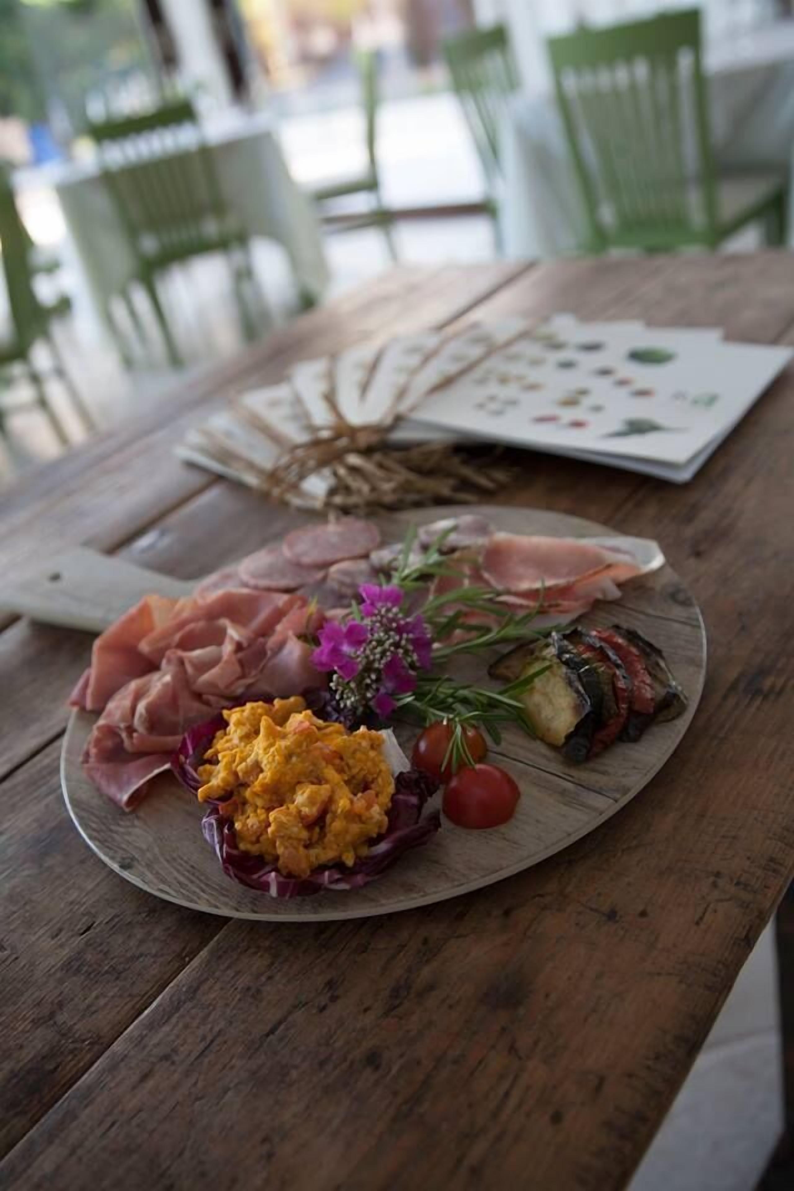 A wooden table with a plate of food, including sliced meats, scrambled eggs, and vegetables, and a decorative branch.