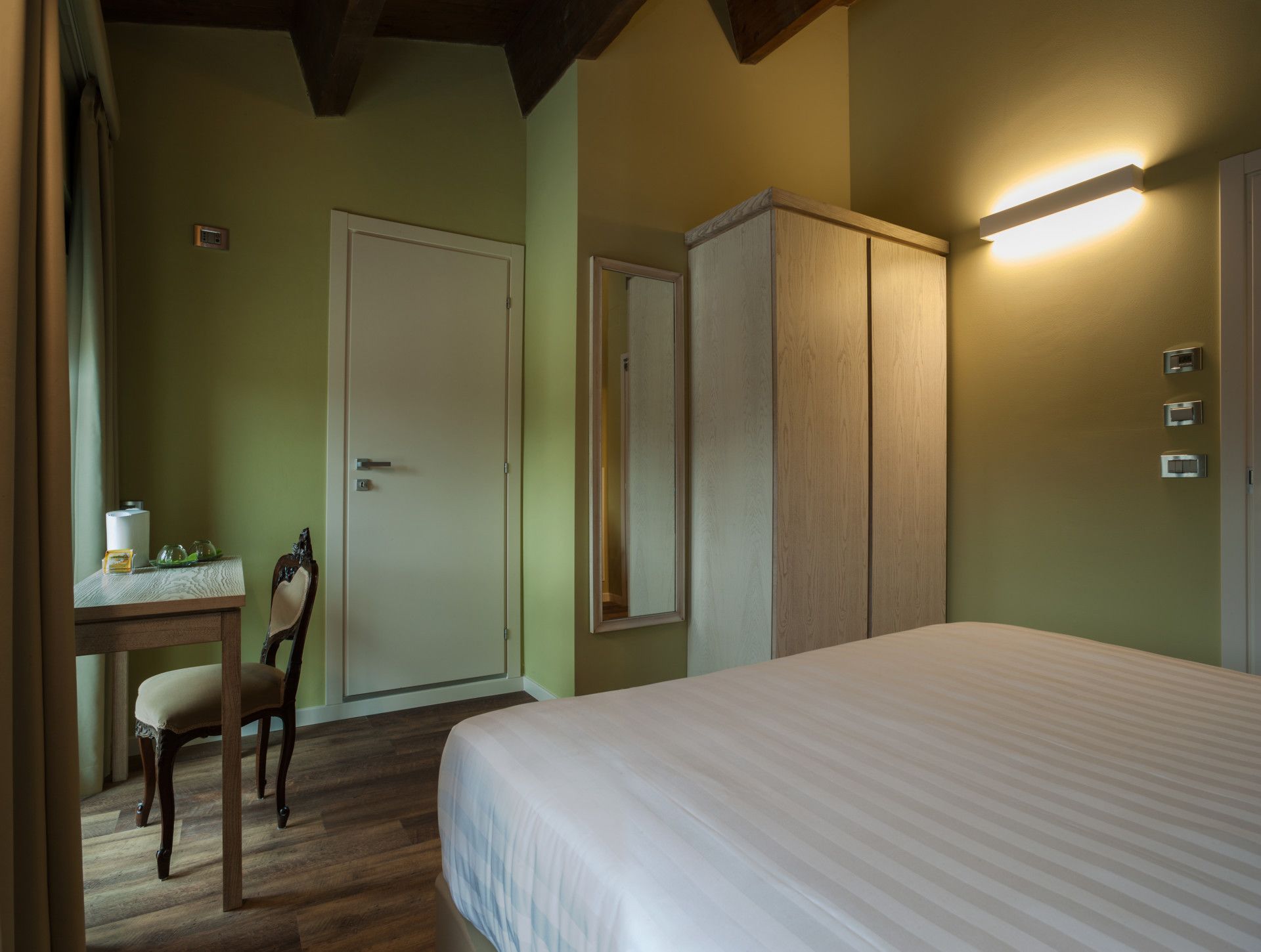Un dormitorio con cama, un escritorio con silla, un armario y una lámpara fijada a la pared.