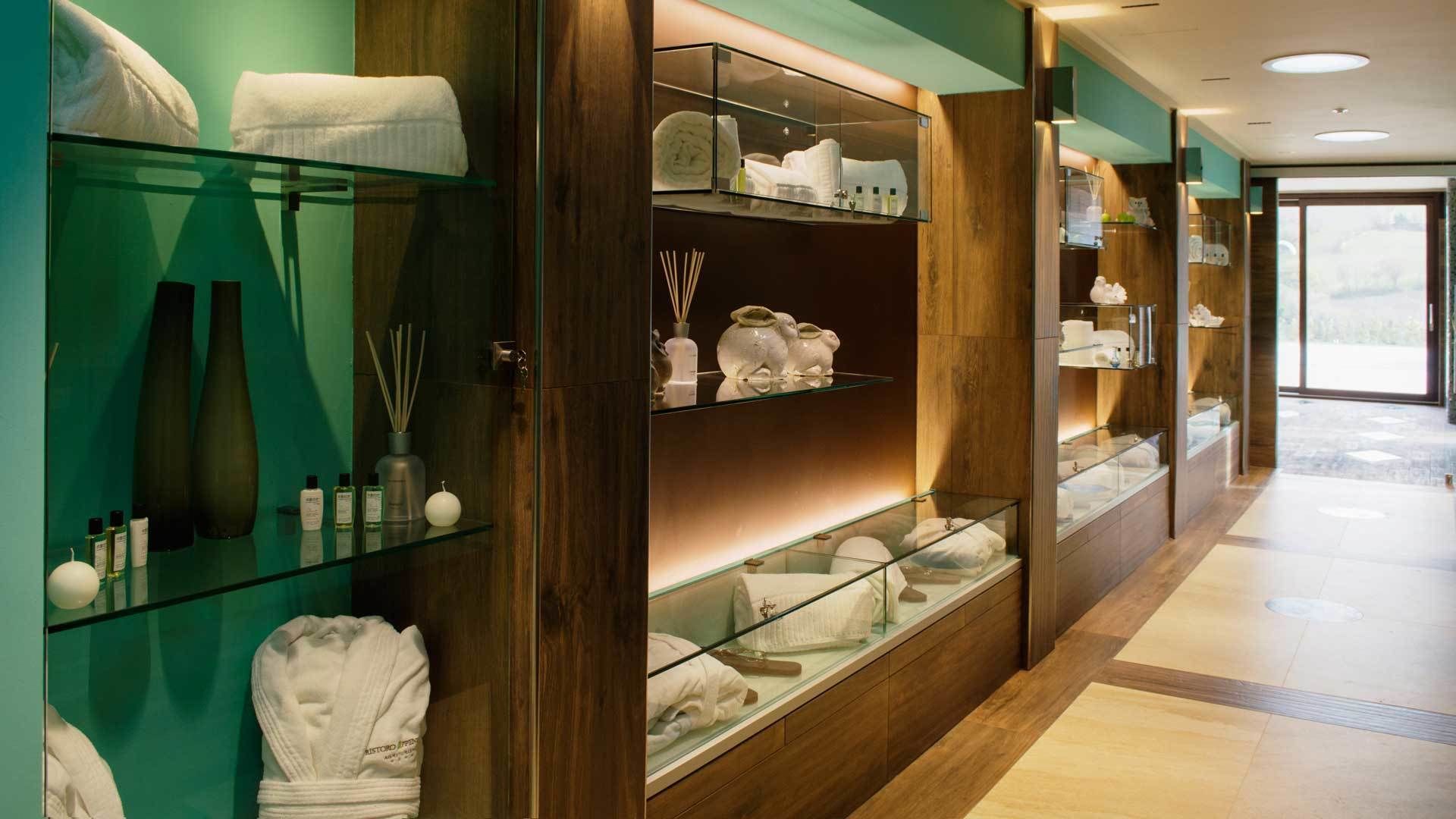 Un hall de hotel con vitrinas de vidrio que contienen artículos de aseo y toallas, paneles de madera y vistas al exterior.