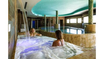A spa area with a hot tub and a pool, surrounded by stone walls and a glass enclosure.