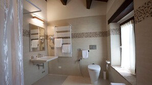 A modern bathroom with a bathtub, toilet, and sink. There are multiple towel racks and a shower area.