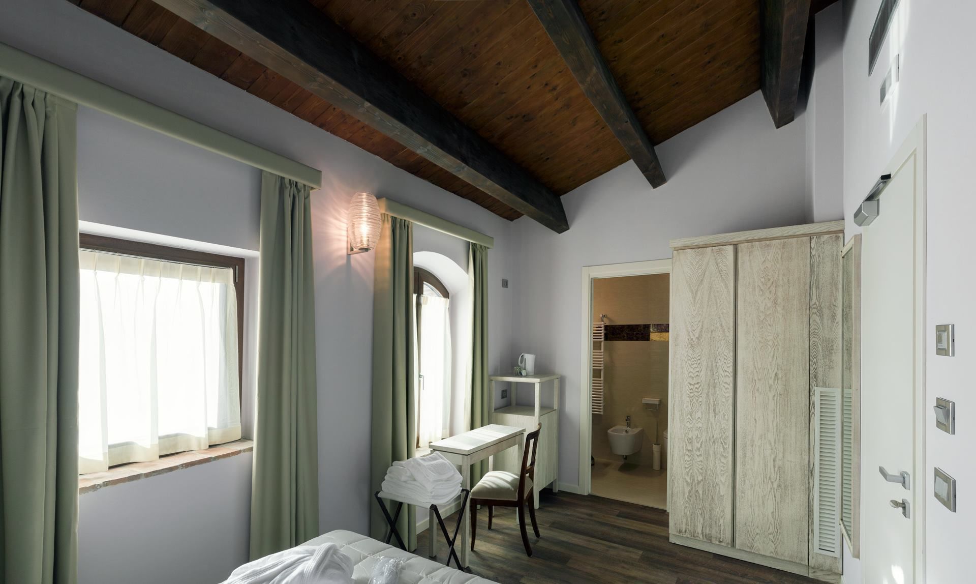 A bedroom with a wooden ceiling, a bed, a desk, and a wardrobe.
