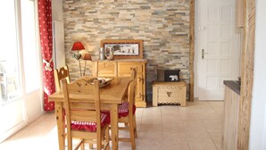 Uma mesa de jantar de madeira com cadeiras, toalha xadrez vermelha e branca, um abajur vermelho, um quadro emoldurado e um aparador de madeira em uma parede de pedra.