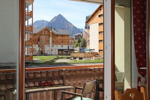 Uitzicht vanaf een balkon met houten meubels, een berg op de achtergrond en gebouwen met balkons.