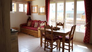 Um quarto aconchegante com uma mesa de jantar de madeira, cadeiras, um sofá e uma janela com cortinas.