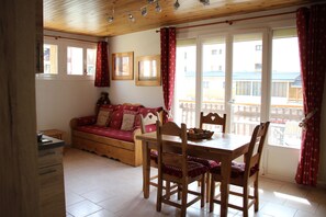 Een gezellige kamer met een houten eettafel, stoelen, een bank en een raam met gordijnen.