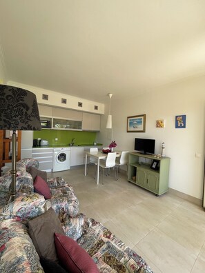 Un espacio habitable compacto con sofá, mesa de comedor, televisor y kitchenette.