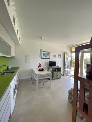 A modern kitchen with a dining area, a washing machine, and a TV.