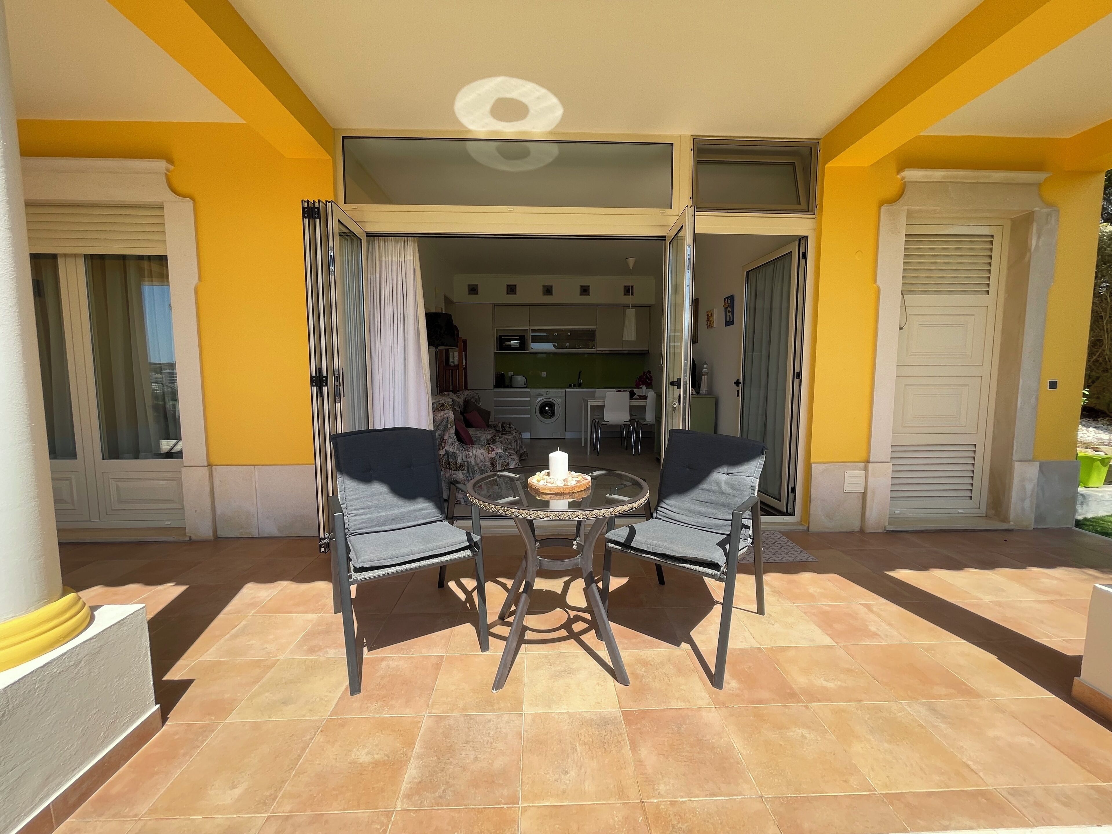 An open patio with a table and chairs, a sliding glass door leading to a kitchen, and a yellow exterior wall.