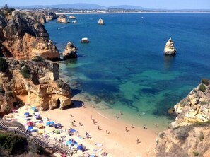 A coastal beach with clear water, rocky cliffs, and a sandy shore with umbrellas. - Cosy Apartment near the beach - Enjoy the summer almost all year (Lagos)