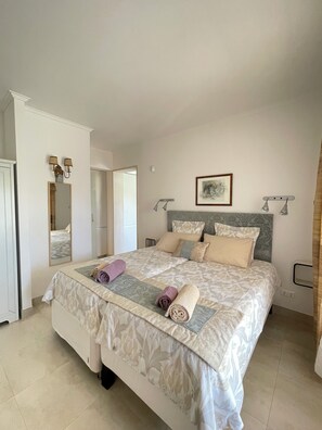 A neatly made bed with a floral bedspread, a headboard with a framed artwork, and a bedside table with a lamp. - Cosy Apartment near the beach - Enjoy the summer almost all year (Lagos)