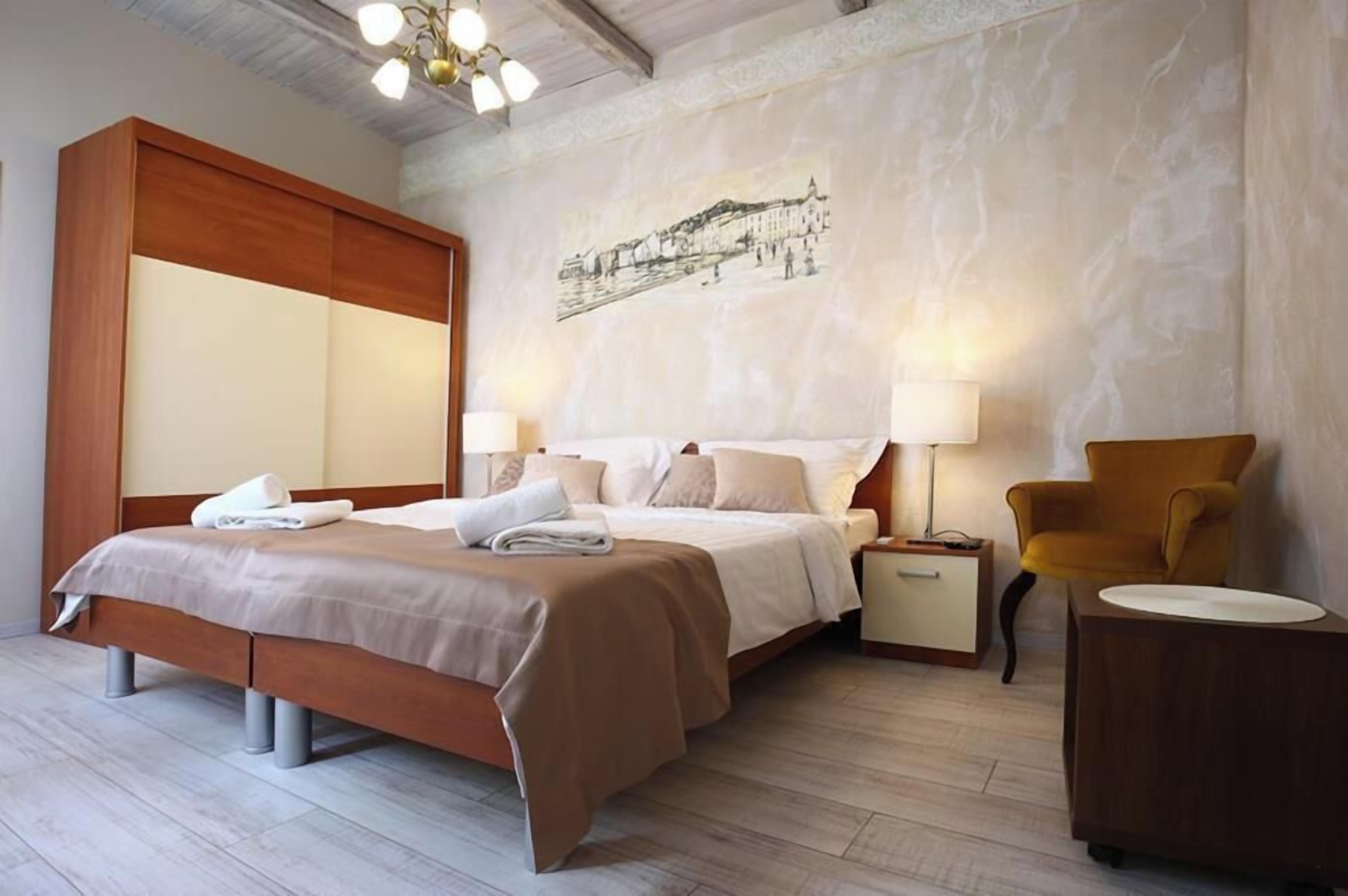 A hotel room with a bed, bedside tables, a chair, and a wall with a cityscape artwork.