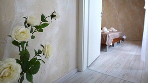 A hallway with a white wall and a door leading to a room with a bed and a small table.