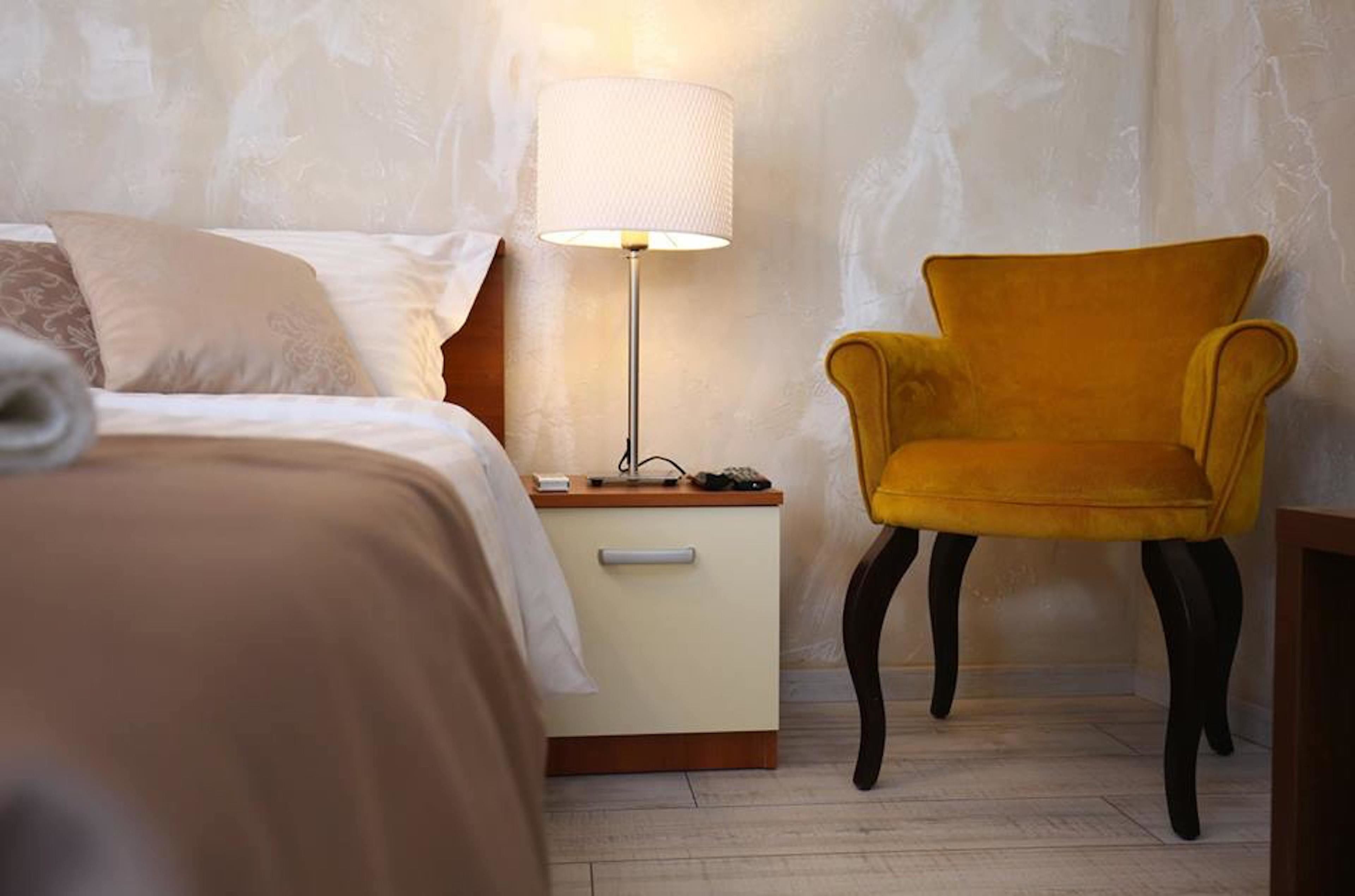 A neatly made bed with a lamp and a chair in a room with patterned wallpaper.