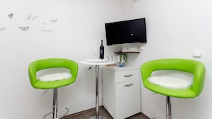 A small room with two green chairs, a white cabinet, a TV, and a wall-mounted shelf.
