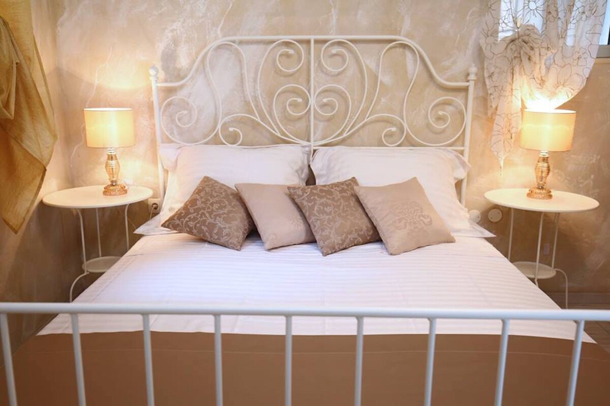 A bed with a white metal frame, a white headboard with a decorative design, and two bedside tables with lamps.