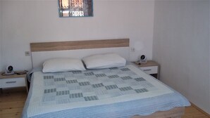 Una cama con cabecera de madera, almohadas blancas y colcha con estampado de cuadros.
