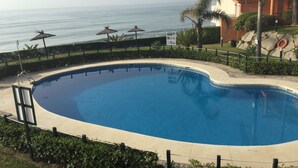 A swimming pool with a curved edge, surrounded by a low fence, and a view of the ocean in the background.