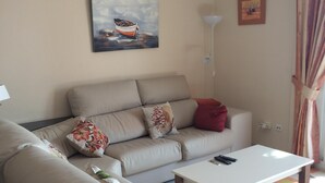 A living room with a beige sofa, a white coffee table, and a painting of a boat on the wall.
