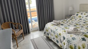 A hotel room with a bed, a chair, a desk, and a view of the outside.