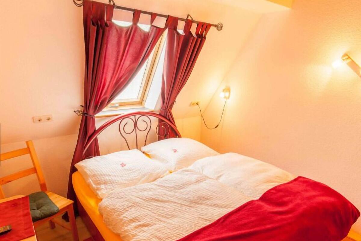 Un lit simple avec un baldaquin, une table de chevet, une chaise et une petite table avec une télécommande.