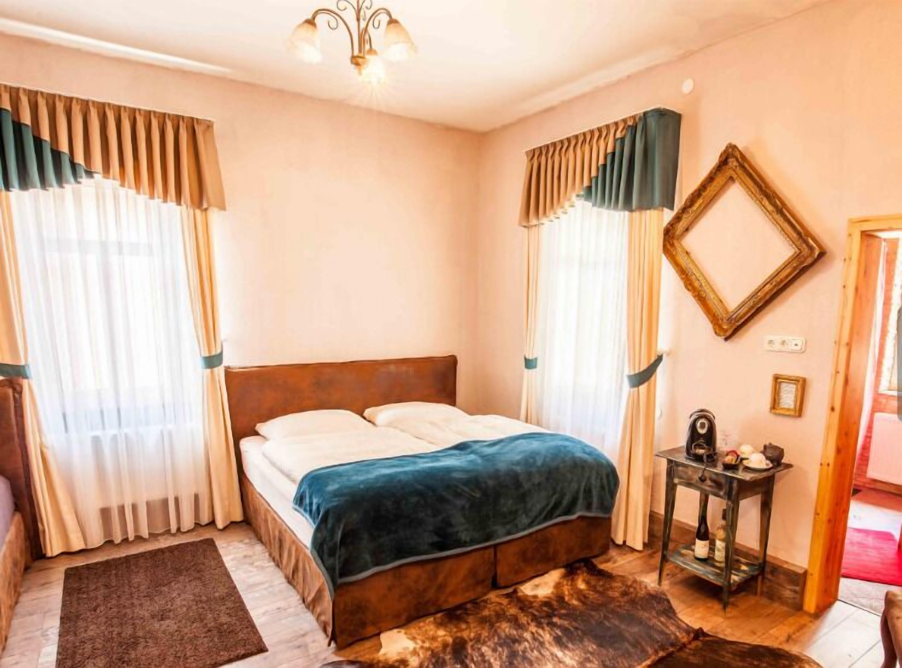 Ein Schlafzimmer mit Bett, Vorhängen, einer Deckenleuchte, einem Spiegel und einem kleinen Tisch mit Gegenständen darauf.