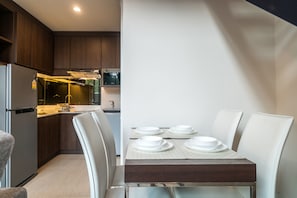 Cozinha moderna com armários de madeira escura, uma geladeira de aço inoxidável e uma área de refeições com uma mesa posta para quatro pessoas.