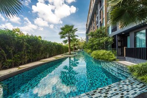 Piscina com borda azulejada, rodeada por vegetação e um edifício com vários andares.