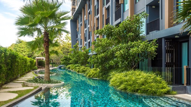 Um edifício moderno com piscina, rodeado por vegetação exuberante e palmeiras.