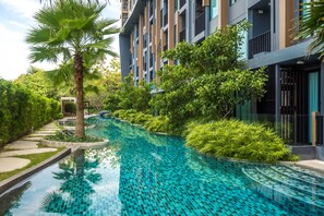 A modern building with a swimming pool surrounded by lush greenery and palm trees. - Aristo Surin by Lofty (Choeng Thale)