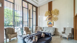 Uma sala de estar ampla, com um sofá azul grande, várias poltronas e um objeto decorativo na parede.