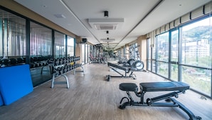 Uma academia com equipamentos de ginástica, grandes janelas e vista para edifícios.