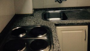 Una cocina con gabinetes blancos, un lavamanos de acero inoxidable y una estufa eléctrica doble.