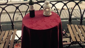 Una mesa con una botella de vino y un farol en un balcón con vista a un río y barcos.