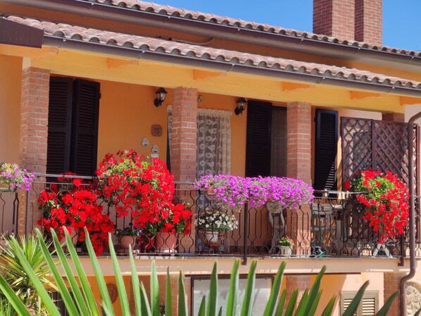 A building with a yellow facade, red flowers in pots, and a tiled roof.