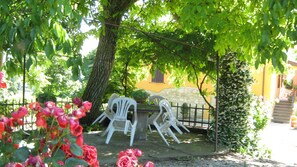 Un'area giardino con tavolo e sedie sotto un albero, circondata da un muro di pietra e una recinzione.