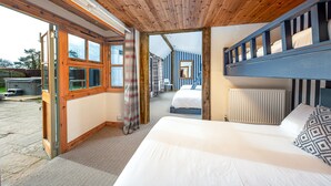 A room with a wooden ceiling, a bed with white bedding, a blue headboard, and a view through an open door to another room with striped walls. - Beautiful cabin near Bath with heated swimming pool sleeps up to 17 people (Bristol)