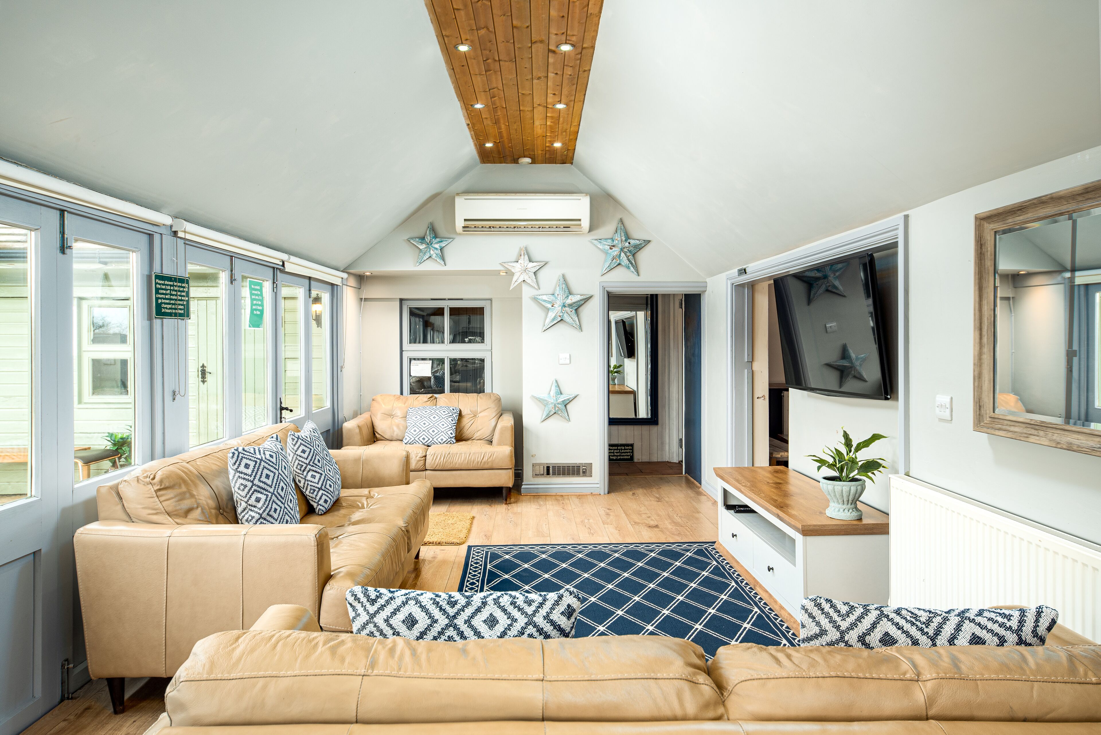 A spacious living area with a high ceiling, a sofa set, a wooden coffee table, and decorative star-shaped wall hangings. - Beautiful cabin near Bath with heated swimming pool sleeps up to 17 people (Bristol)
