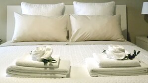 A hotel room with a large bed, two pillows, a folded towel, and a painting on the wall.