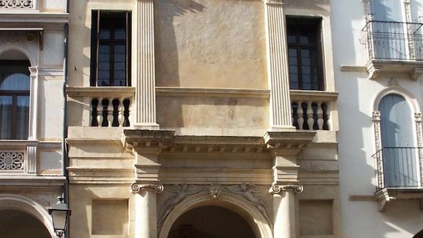 A classical building facade with a central archway, flanked by columns and pilasters, and a balcony on the upper floor.