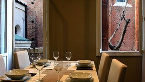 A dining table set with plates, glasses, and cutlery, with a view of a brick building through a window.