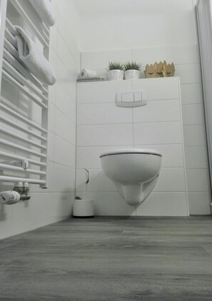 A modern bathroom with a white toilet, a towel rack, a radiator, and a small potted plant on the wall.