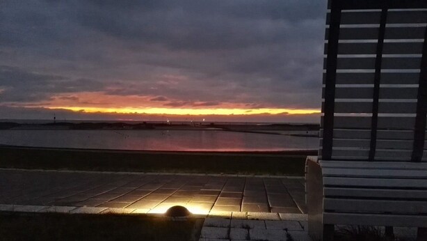 Vista del atardecer desde un paseo marítimo con un banco.