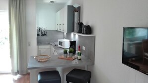 Una cocina moderna con microondas, cafetera y una planta pequeña en la encimera. Hay dos taburetes negros y una cesta en la encimera.